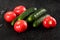 Spraying water on fresh raw gherkins small cucumber with bumpy skin and pink tomatoes on black background with waterdrops