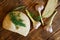 Sprigs of dill, garlic and a loaf of white round bread lie on a rustic wooden table made of pine boards. Summer still life