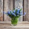 Spring bluebell flowers in small vase on wooden background. Still life