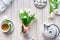 Spring celebration flat lay. Female hands with white tulips, sweets and tea on white wooden table. Spring celebration flat lay.