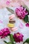 Spring composition flatlay: colorful macaroons with purple and pink peonies, green leaves on a light concrete background and a pin