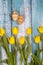 Spring composition of yellow flowers and eggs with a painted cute face on a blue background. Congratulations on Easter