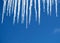 Spring drops from long crystal icicles hanging down before clear blue sky on bright sunny day closeup