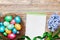 Spring holiday greeting card on Easter with empty notebook for recipe, nest with colorful eggs and flowers on rustic wooden table.
