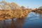 Spring industrial landscape. River, clear blue sky, crowns of trees without leaves and enterprise with pipes.