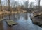 Spring landscape with a small wild river, bare trees without leaves, old board platform in a flooded river