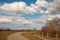 Spring landscape with trees and blue sky with white clouds. A footpath walkway in the park passes by the bench