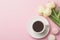 Spring morning concept. Flat-lay of cup of coffee with white flowers and macarons over light pink background, top view with space