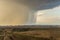 Spring natural and urban panoramic landscape with approaching huge storm cloud and heavy rain over burnt field and large city on