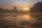 Spring nature landscape at dawn in foggy morning with bright sun on horizon. Amazing sunrise on river shore at mist. Natural scene