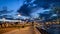 Spring night city on pier promenade people  walk relaxing street lamp light reflection on blue sky and sea water  tree branch and