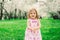 Spring portrait of cute little toddler girl in blue jeans dress walking in blooming park