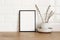 Spring still life. Blank black picture frame mockup on wooden table background. Easter composition with blooming goat willow,