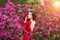 Spring touch. Happy beautiful young woman in red dress enjoy fresh pink flowers and sun light in blossom park at sunset.