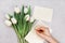 Spring tulip flowers and man hand signing a card on gray stone table top view in flat lay style. Greeting for Womens or Mothers Da