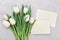 Spring tulip flowers and paper card on gray stone table top view in flat lay style. Greeting for Womens or Mothers Day.