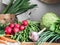 Spring vegetarian food ingredient variety. Assortment of spring vegetables for healthy cooking over rustic cupboard, white wall