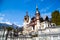 Spring view of Peles Castle with snowy Bucegi Mountains in the background.