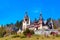 Spring view of Peles Castle with snowy Bucegi Mountains in the background.