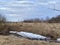 Spring village landscape: cloudy sky, dry grass and large white ice floes on the field