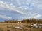 Spring village landscape: cloudy sky, dry grass and large white ice floes on the field