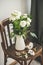 Spring white buttercup flowers in enamel jug on wooden chair