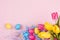 Springtime easter festive background - homemade painted multicolored eggs, tulips bouquet on pastel light pink background.