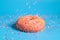 Sprinkles falling from top on Tasty pink strawberry donut. Delicious dessert on blue background.