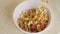 Sprinkling muesli granola with dry fruit and raisin into bowl for healthy breakfast closeup. Adding cereal to