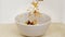 Sprinkling muesli granola with dry fruit and raisin into bowl for healthy breakfast closeup. Adding cereal to