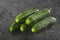 Sprinkling water over five green fresh small cucumbers gherkins on a black background with waterdrops