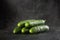 Sprinkling water over five green fresh small cucumbers gherkins on a black background with waterdrops