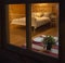 Spy view through window of wooden country house, made bed, set table for a romantic dinner, a glass of wine and plates, a secret