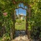 Square Arched wooden arbor at the entrance of a garden with playhouse slides and swings