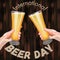 Square banner with two hands holding pilsner glasses with beer on wooden background. Light beer with foam. International