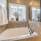 Square Bathtub and shower stall of warm toned bathroom with tiled wall and floor