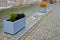 square bordered by concrete look flowerpots with flowers and