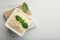 Square bowl with grated parmesan cheese and basil on white table, top view. Space for text