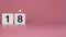 A square candle saying the number 18 being lit and blown out on a pink background celebrating a birthday