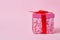 Square cardboard pink box tied with a red bow on a pink background