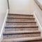 Square Carpeted indoor staircase of home with brown handrail against white side wall