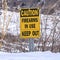 Square Caution Firearms In Use Keep Out sign on a mountain covered with snow in winter