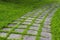 Square concrete pavement walkway overgrown with grass