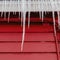 Square crop Spiked frozen icicles at the roof of home with vibrant red wooden exterior wall