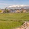 Square Damaged curving road amid grassy terrain against homes and snow capped mountain