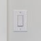 Square Electrical rocker light switch on white wall against blurry door background