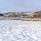 Square Field with snow in winter with homes on snowy hill against sky backgdrop