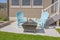 Square fire pit and blue plastic chairs on the yard of a home on a sunny day
