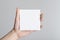 Square Flyer / Invitation Mock-Up - Male hands holding a blank flyer on a gray background