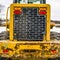 Square Focus on the rear of an old yellow bulldozer against snowy ground and cloudy sky